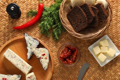 Photo of Tasty butter, dill, chili peppers and rye bread on wicker mat, flat lay