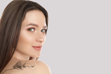 Image of Smiling young woman with beautiful flower tattoo on light background, space for text
