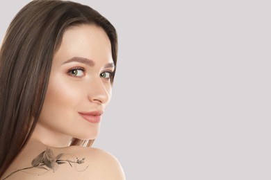 Smiling young woman with beautiful flower tattoo on light background, space for text