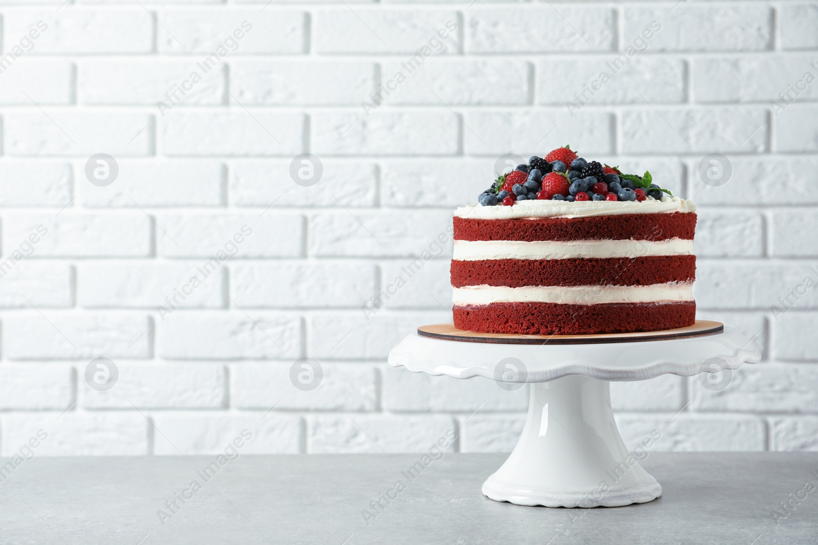 Photo of Stand with delicious homemade red velvet cake and space for text on brick wall background