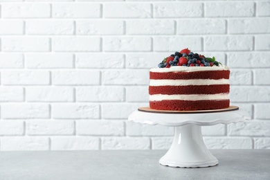 Stand with delicious homemade red velvet cake and space for text on brick wall background