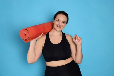 Happy overweight woman with yoga mat on light blue background