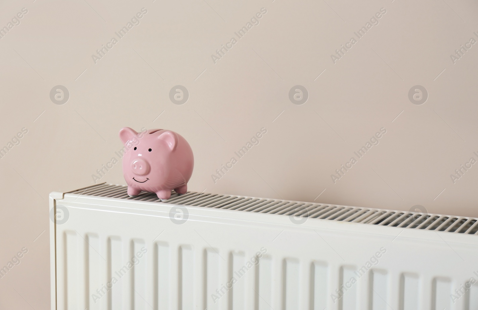 Photo of Piggy bank on heating radiator against light background