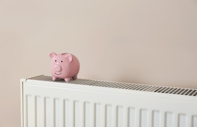 Piggy bank on heating radiator against light background