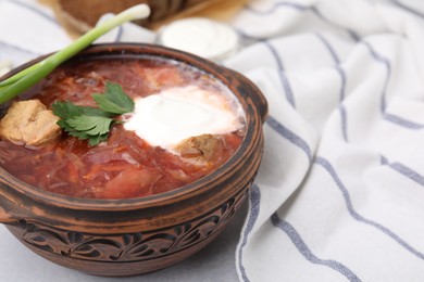 Photo of Tasty borscht with sour cream in bowl served with green onion on light grey table, closeup. Space for text