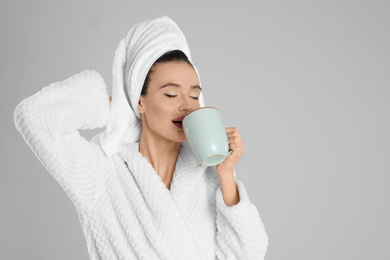 Photo of Beautiful young woman in bathrobe with cup of coffee on light grey background. Space for text