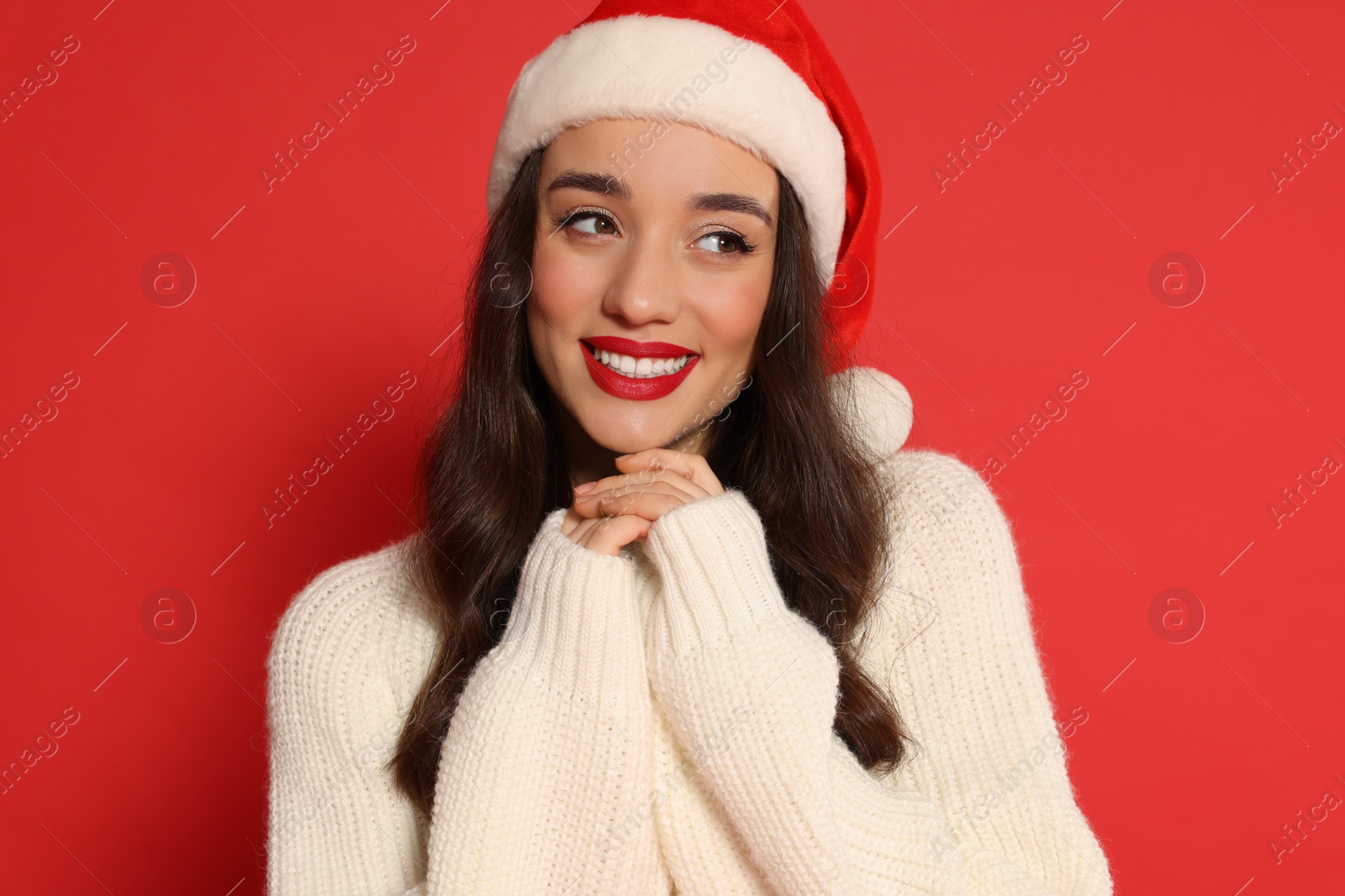 Photo of Christmas celebration. Beautiful young woman in Santa hat on red background