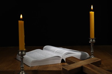 Photo of Bible, cross and church candles on wooden table