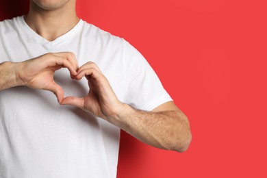 Photo of Man making heart with hands on red background, closeup. Space for text