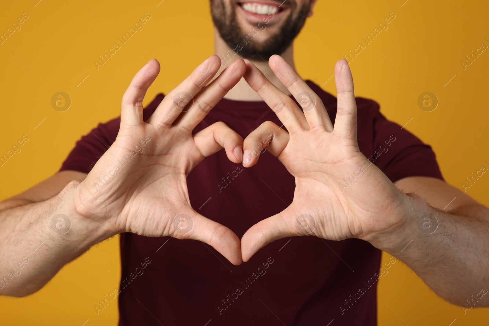 Photo of Man making heart with hands on yellow background, closeup