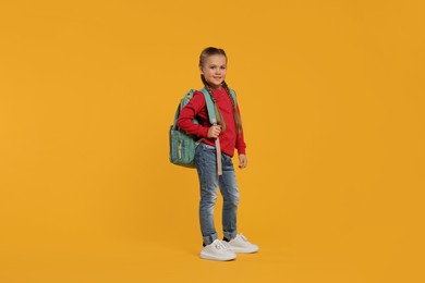 Photo of Happy schoolgirl with backpack on orange background