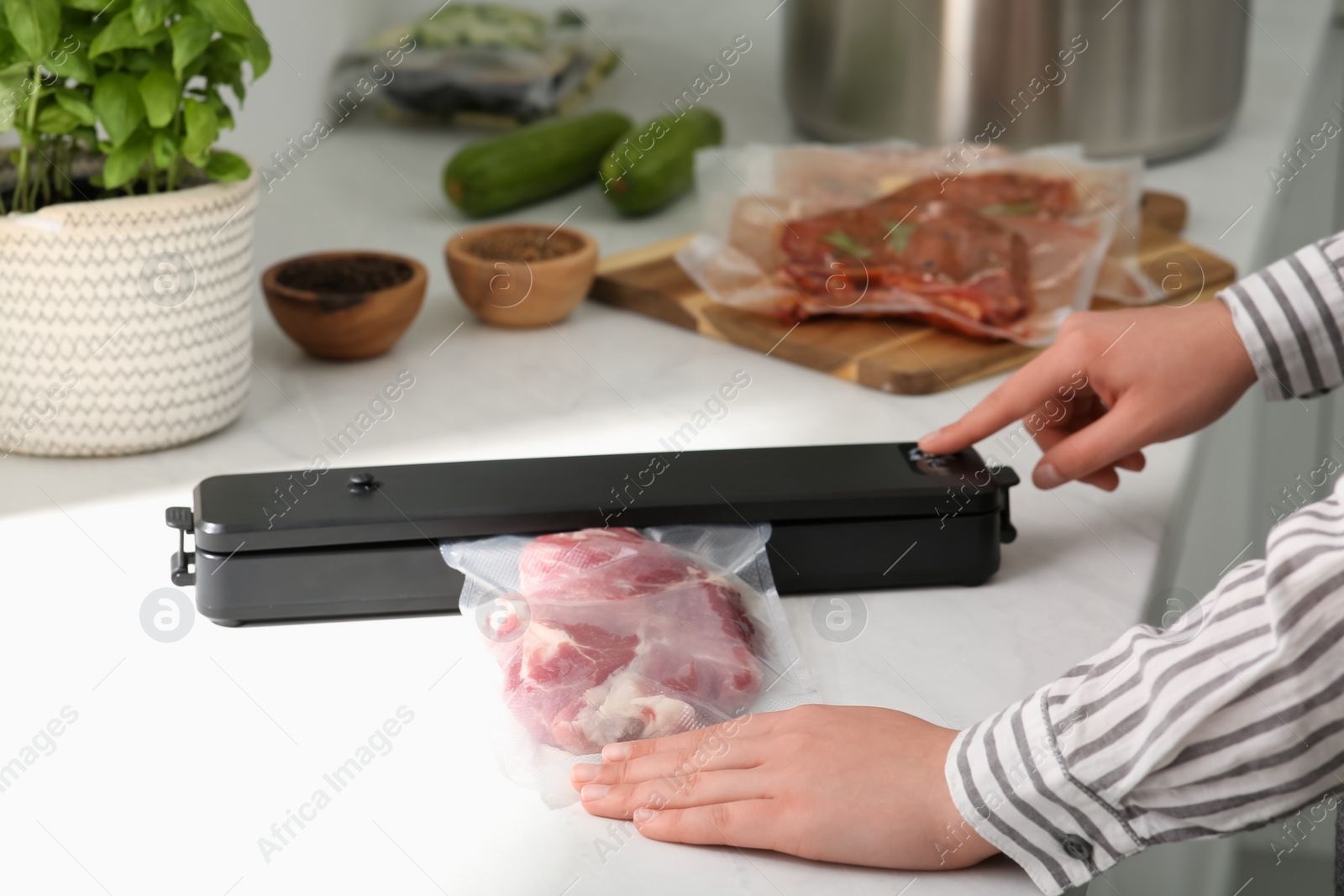 Photo of Woman using sealer for vacuum packing in kitchen, closeup. Sous vide cooking