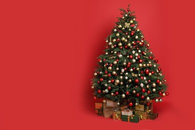 Photo of Beautifully decorated Christmas tree and many gift boxes on red background, space for text