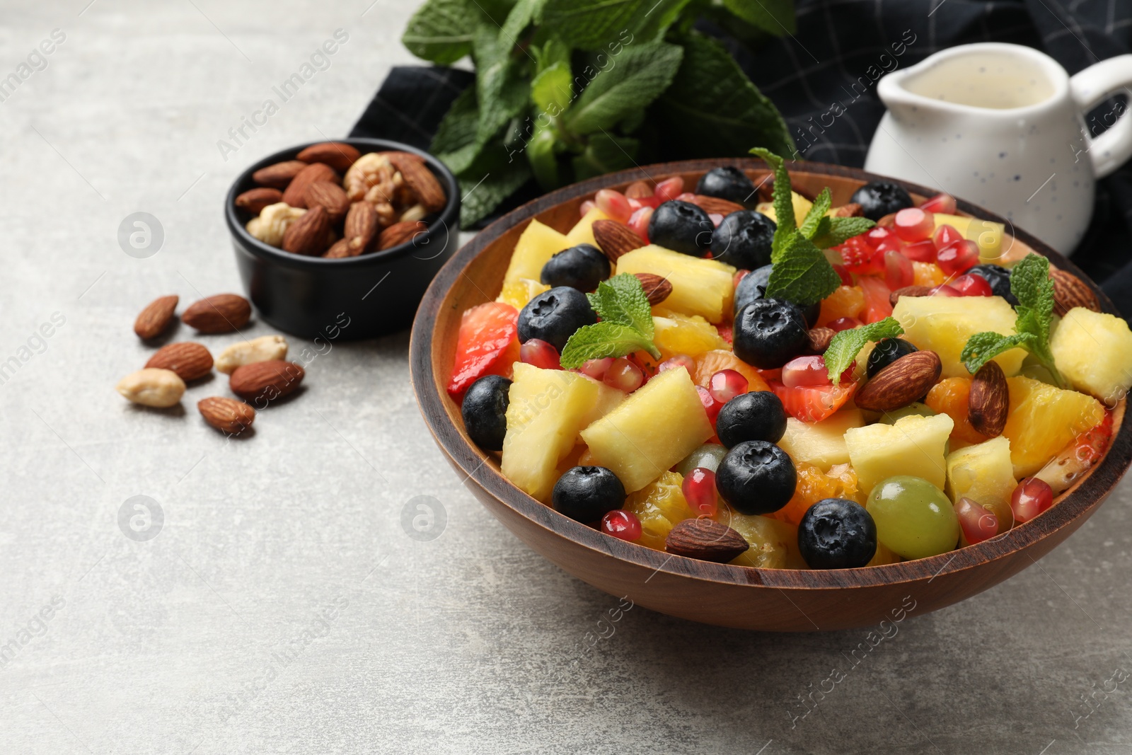 Photo of Delicious fruit salad in bowl, nuts and fresh mint on grey table. Space for text