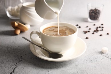 Photo of Pouring milk into cup with coffee on light grey textured table, closeup