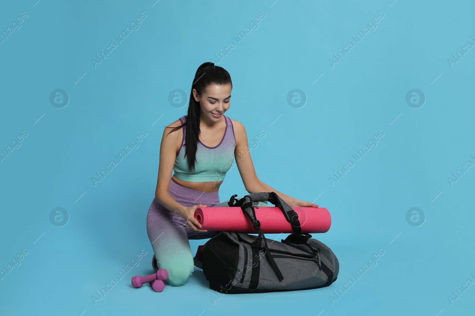 Photo of Beautiful woman with sports bag and yoga mat on light blue background