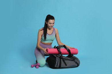 Beautiful woman with sports bag and yoga mat on light blue background