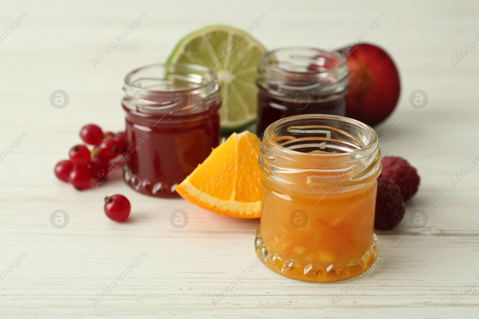 Photo of Jars of different jams and ingredients on white wooden table