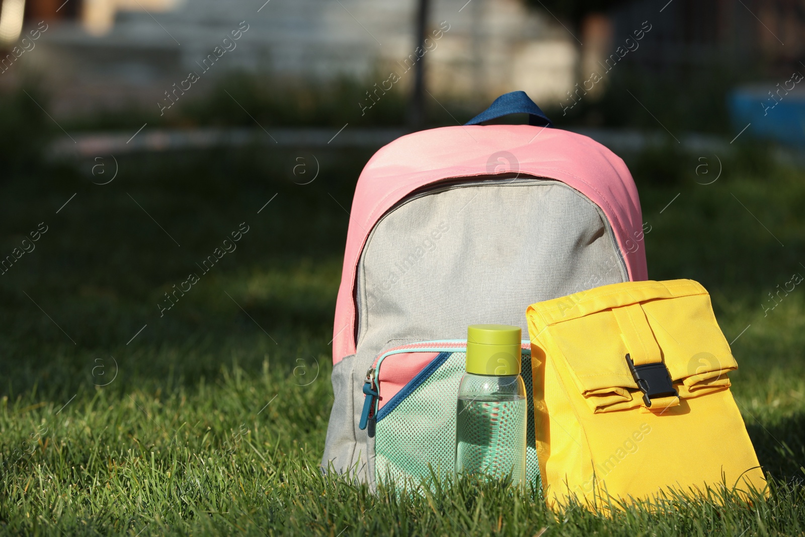 Photo of Backpack, lunch bag and bottle of water on green grass outdoors, space for text