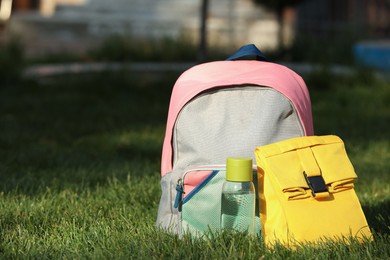 Photo of Backpack, lunch bag and bottle of water on green grass outdoors, space for text