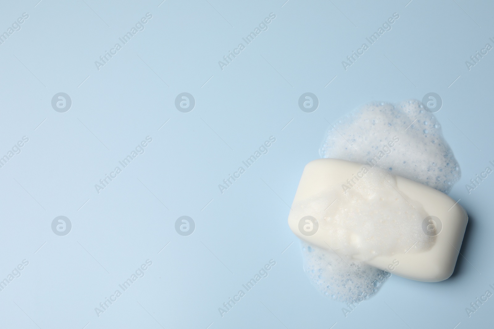 Photo of Soap and fluffy foam on light blue background, top view. Space for text