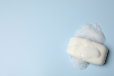 Photo of Soap and fluffy foam on light blue background, top view. Space for text