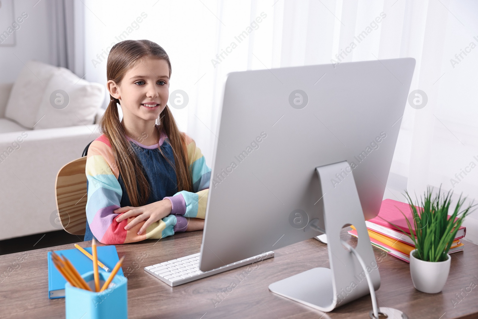 Photo of E-learning. Cute girl using computer during online lesson at table indoors