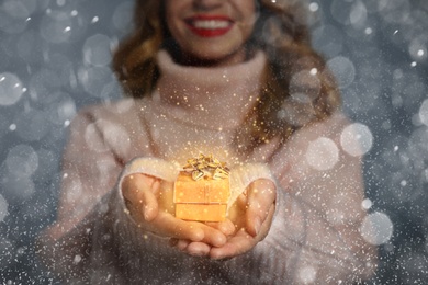 Image of Young woman with small Christmas gift against grey background, focus on hands