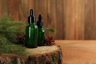 Photo of Pine essential oil, cones and branches on wooden table. Space for text