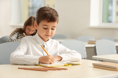 Photo of Portrait of cute little boy studying in classroom at school. Space for text