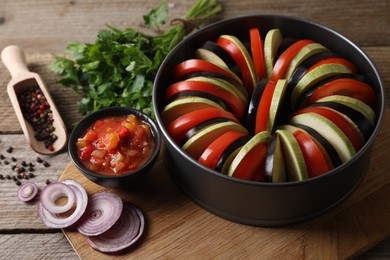 Photo of Cooking delicious ratatouille. Different fresh vegetables and round baking pan on wooden table, closeup
