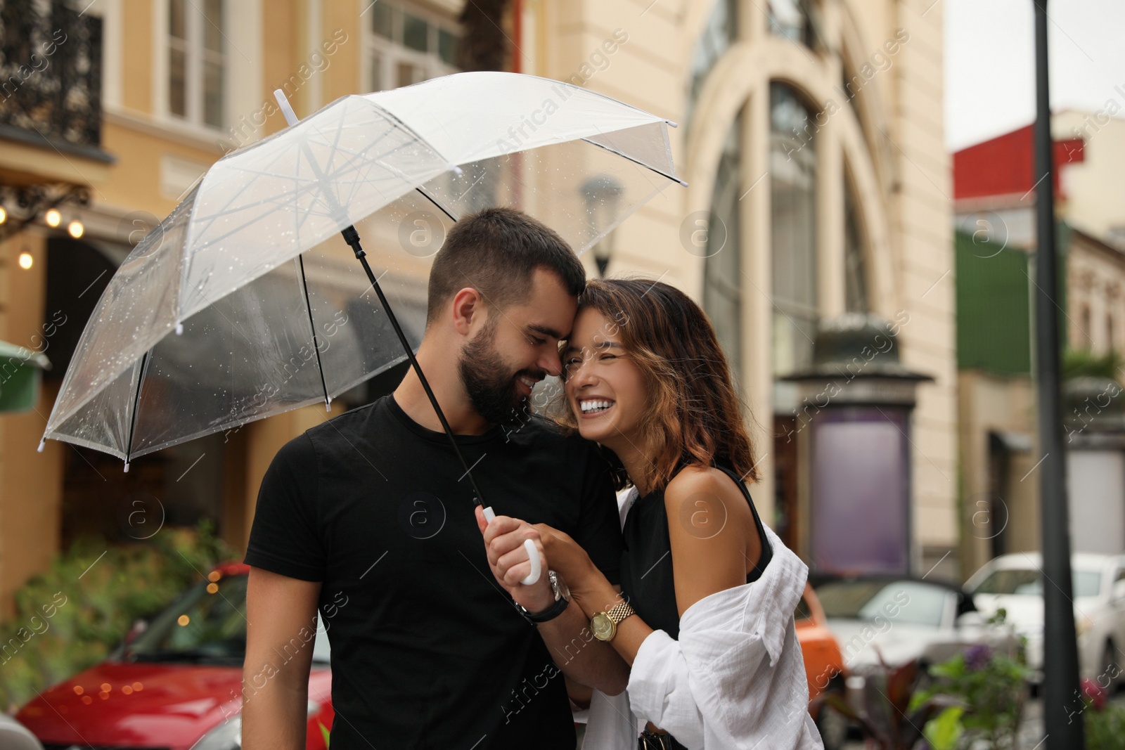 Photo of Young couple with umbrella enjoying time together under rain on city street