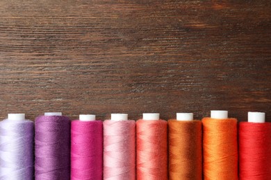 Photo of Set of colorful sewing threads on wooden table, flat lay. Space for text