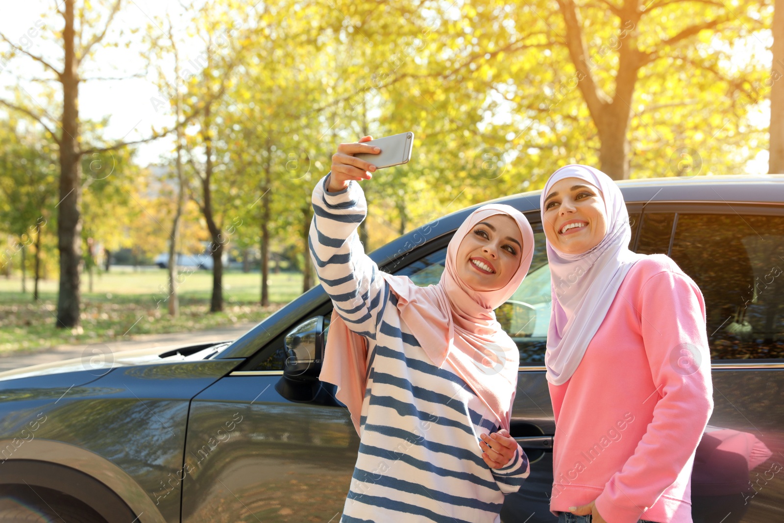 Photo of Muslim women taking selfie near car, outdoors