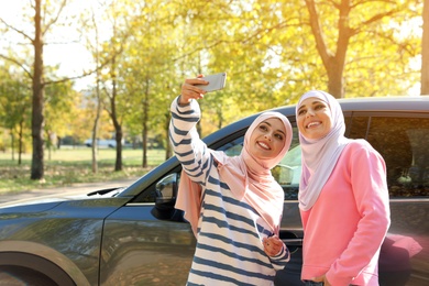 Photo of Muslim women taking selfie near car, outdoors