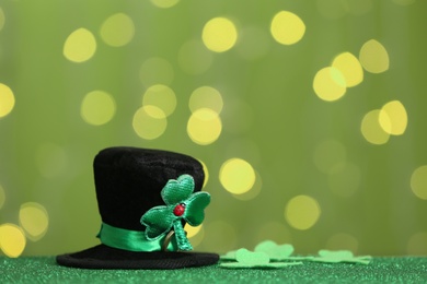 Photo of Leprechaun hat and clover leaves on table against blurred lights, space for text. St Patrick's Day celebration