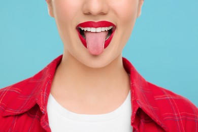 Woman showing her tongue on light blue background, closeup