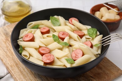 Photo of Tasty pasta with smoked sausage and basil in bowl on table, closeup