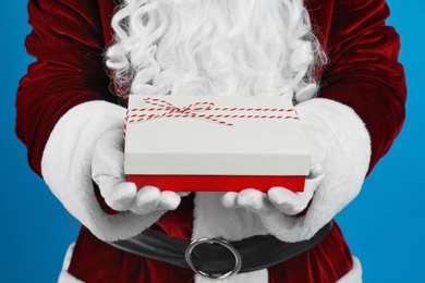 Photo of Santa Claus holding Christmas gift on blue background, closeup