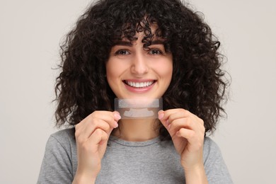 Young woman holding teeth whitening strips on light grey background