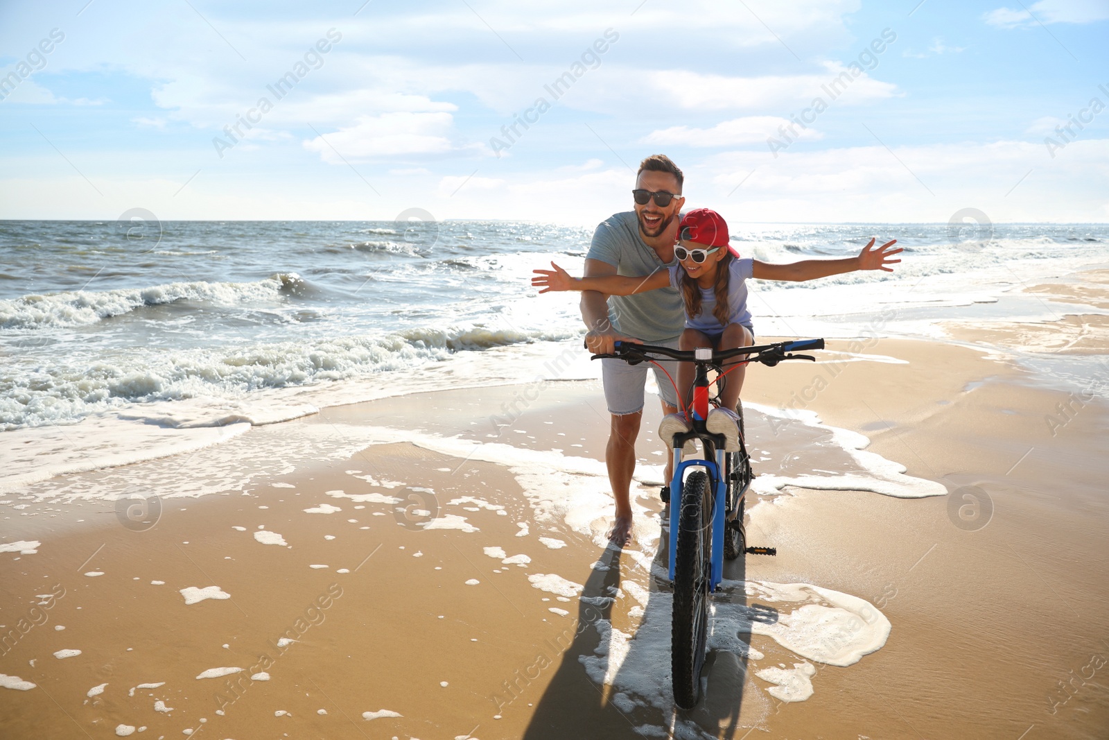 Photo of Happy father teaching daughter to ride bicycle on sandy beach near sea