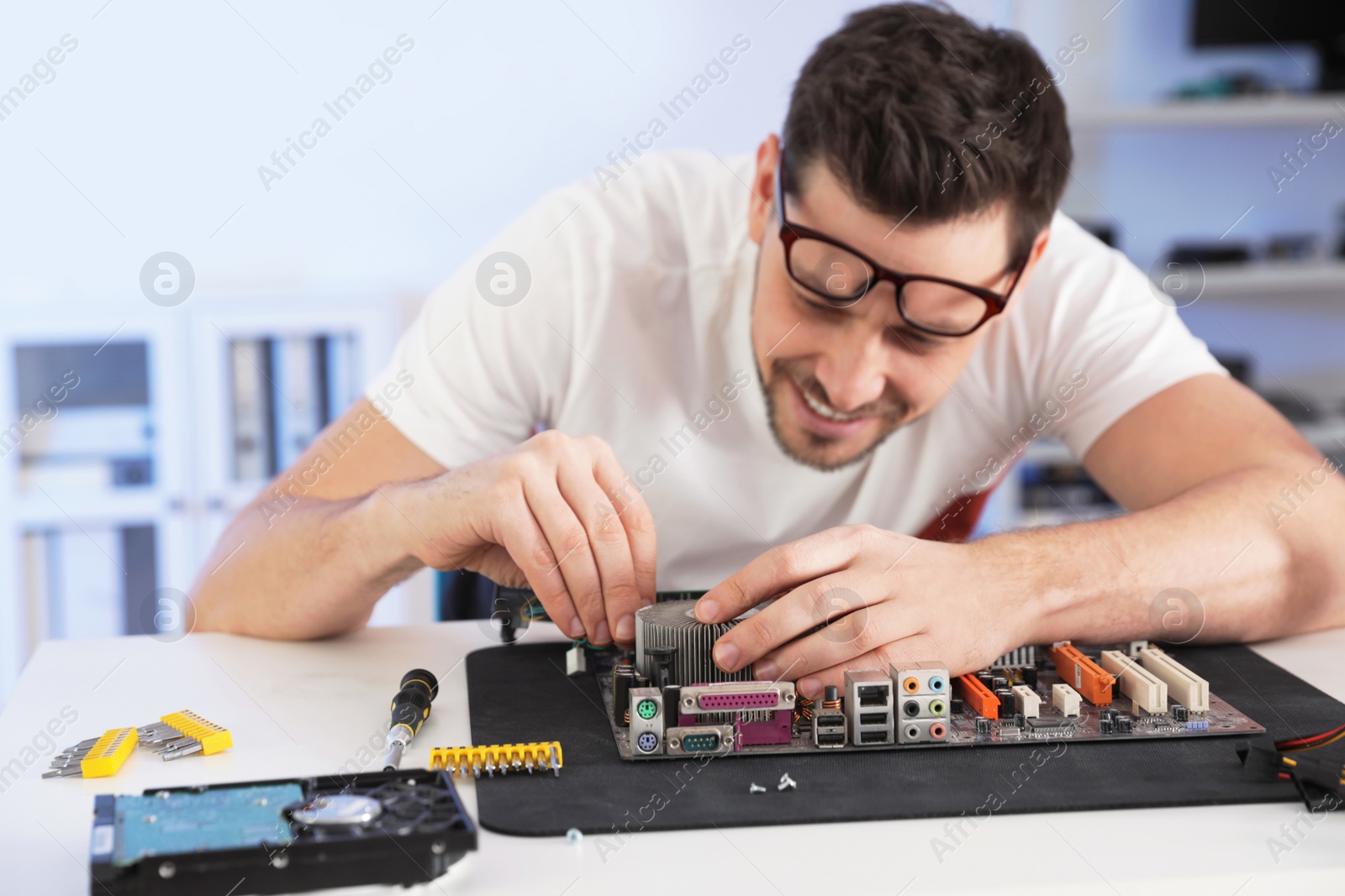 Photo of Male technician repairing motherboard at table indoors