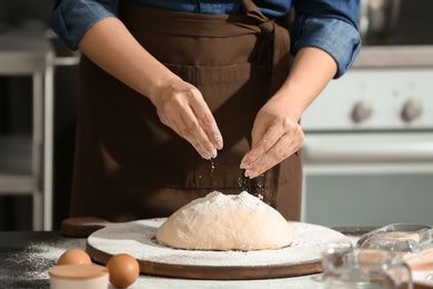 Photo of Woman sprinkling flour over dough on table in kitchen