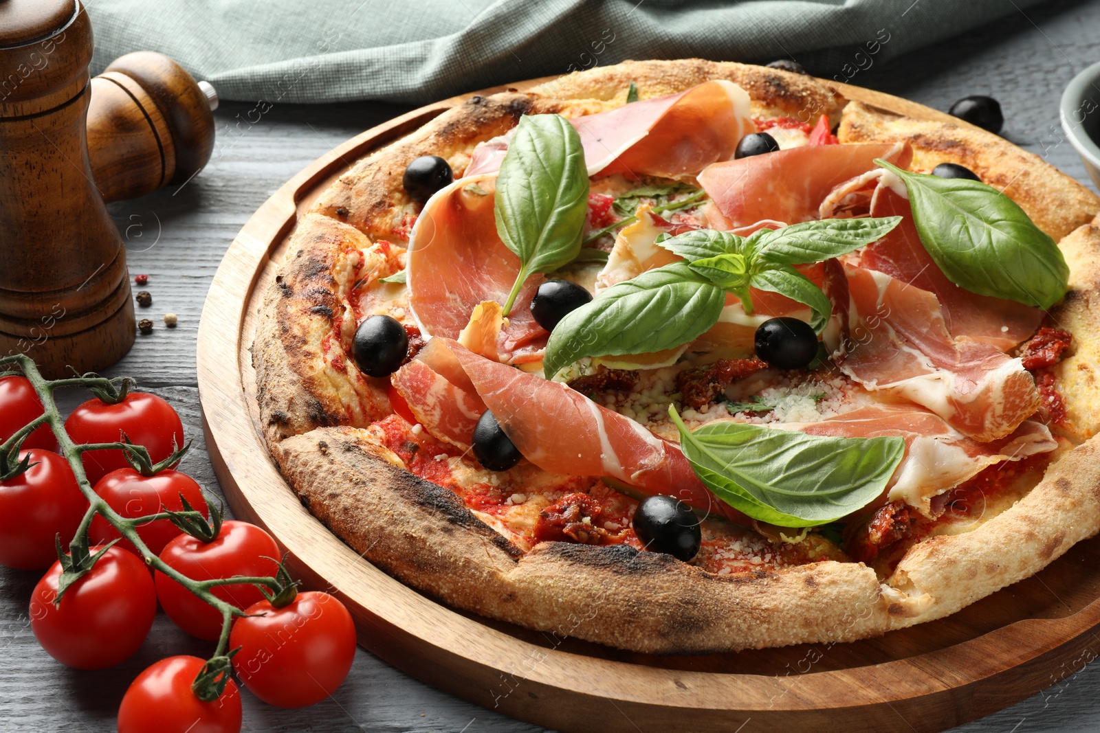 Photo of Tasty pizza with cured ham, olives, tomatoes and basil on gray wooden table, closeup