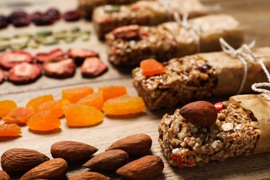 Photo of Different tasty granola bars and ingredients on wooden table, closeup