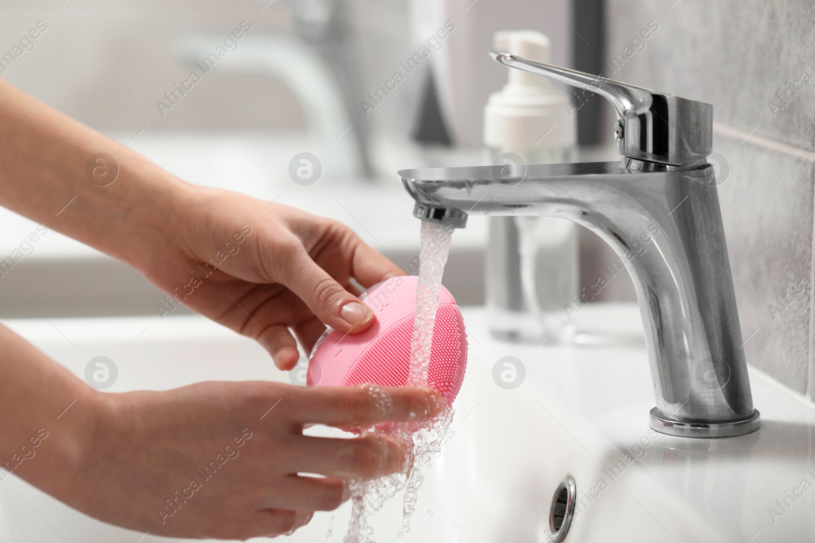 Photo of Young woman washing facial brush in bathroom, closeup