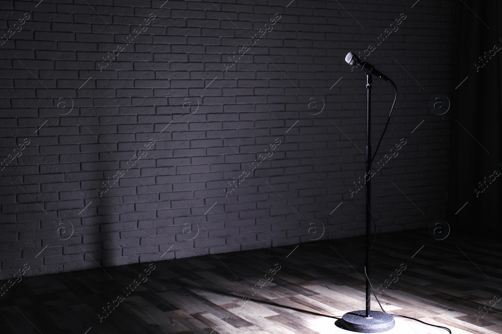 Photo of Microphone on dark stage near brick wall. Space for text