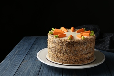 Dish with delicious carrot cake on wooden table against black background. Space for text