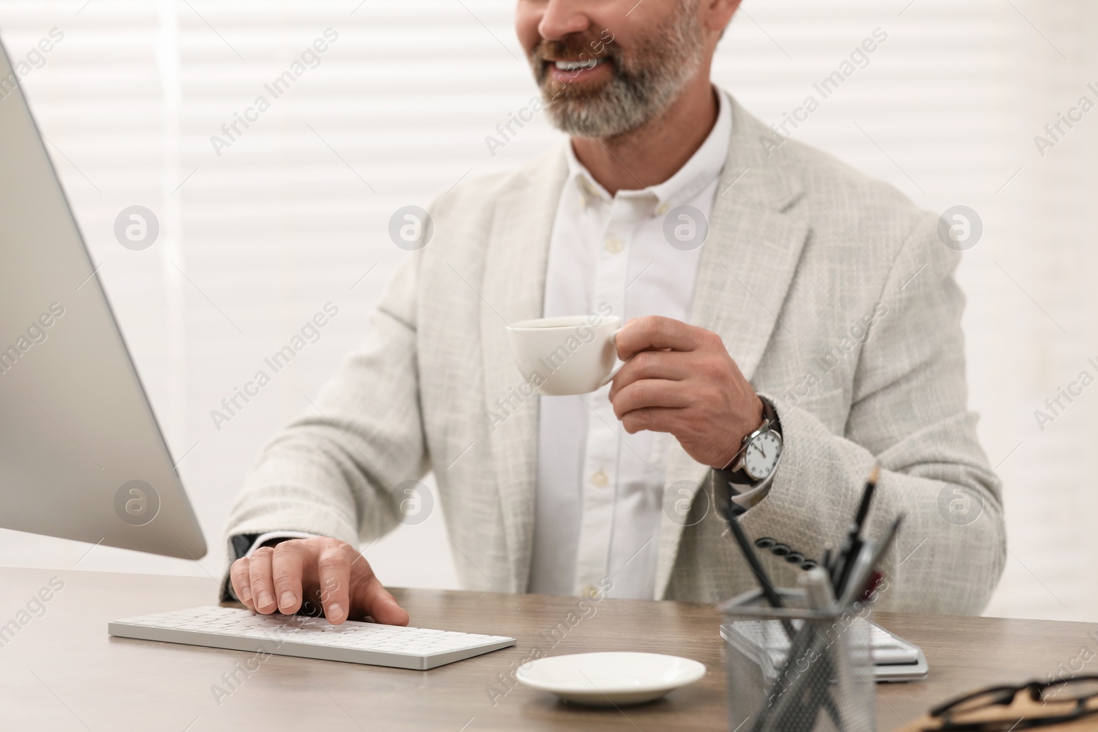 Photo of Professional accountant with cup of coffee working at wooden desk in office, closeup