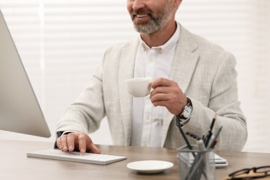Photo of Professional accountant with cup of coffee working at wooden desk in office, closeup